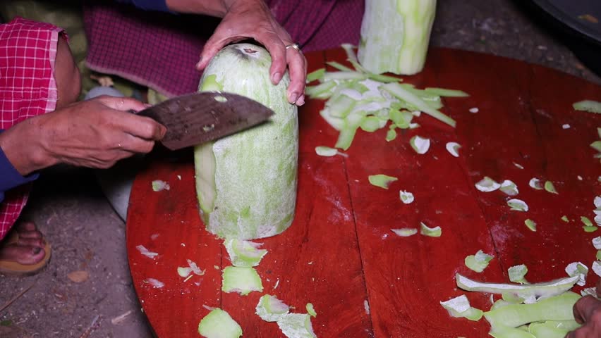 The man hand peeling wax gourd with the knife on the wooden table for the cooking.