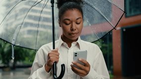 African American woman holding using mobile phone smartphone rain female umbrella texting online internet city typing message technology girl businesswoman business chat cellphone connection outdoor - Powered by Shutterstock - Get 15% off with code: PIKWIZARD15