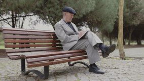 Elderly man writing on notepad while sitting on bench in park - Powered by Shutterstock - Get 15% off with code: PIKWIZARD15