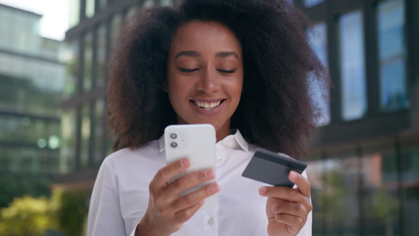 African American woman using mobile phone smartphone bank card online pay internet app finance money female businesswoman buying order shopping business city outside girl technology debit cash credit