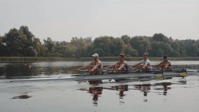Rowing team training. Side view of 4 young caucasian male rowers, during a rowing practice, athlete sitting in a boat in the river Dnipro, rows through a calm water in autumn. 4k footage. City area in - Powered by Shutterstock - Get 15% off with code: PIKWIZARD15