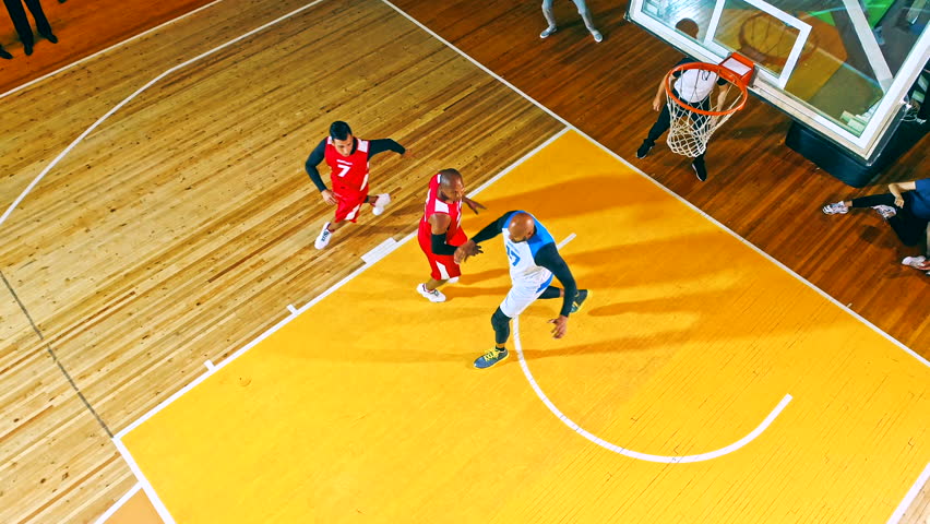Top-down view of a fast-paced basketball game on a vibrant wooden court. Players in red and blue compete for possession, showcasing intense action, teamwork, and athleticism in a dynamic sports moment