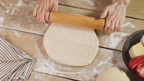 Woman baker is rolling out dough using wooden rolling pin on cozy wooden table. She is rolling dough in flour, preparing it for an Italian pizza with tomato and cheese. - Powered by Shutterstock - Get 15% off with code: PIKWIZARD15