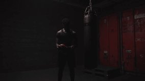 african american athletic man putting on red boxing gloves in a dark room, strong boxer preparing for training and fight - Powered by Shutterstock - Get 15% off with code: PIKWIZARD15