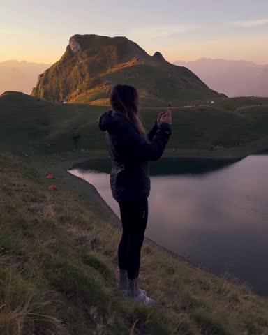 Hiker taking pictures of a sunrise over a mountain lake in the pyrenees