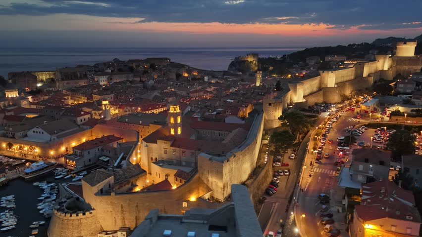 Aerial shot of historic city of Dubrovnik in Croatia, UNESCO World Heritage site. Illuminated streets, buildings and marina with boats. Dubrovnik old town after sunset with city lights. 4K HDR shot 
