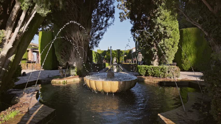 Slow motion gimbal shot of fountain surrounded by trees in Gardens of the Generalife in Alhambra. Granada, Spain. Serene beauty ofGeneralife gardens in Alhambra with stunning fountains 