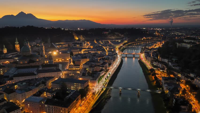 Sunset over Salzburg with illuminated buildings and river reflections. Aerial night view of Salzburg old town, red sunset sky at background, Austria