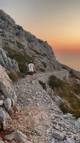 Hiker enjoying breathtaking sunset views over mediterranean sea from rocky mountain path