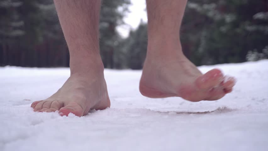 barefoot in the snow, close-up, selective focus. A man walks along a snowy road without shoes.