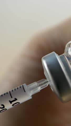 Paramedic hand steadies vial while filling syringe with liquid medication. Medical treatment preparation for effective patient care. Immunization process. Professional medical equipment use 