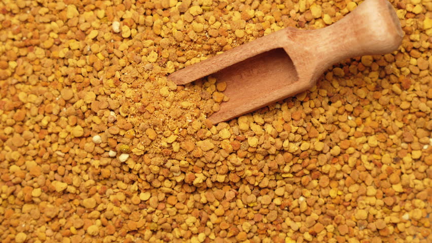A small wooden scoop on a pile of bee pollen granules