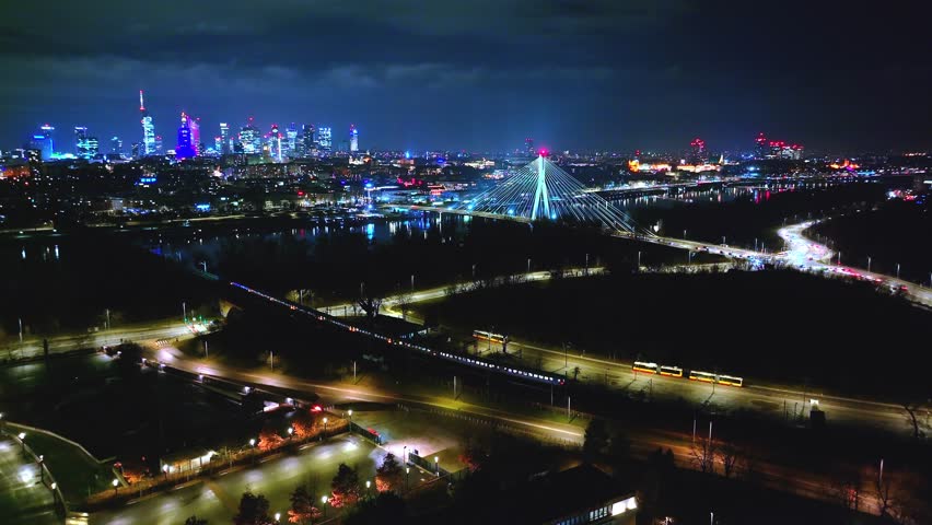 Warsaw at night from the sky—Świętokrzyski Bridge, moving traffic, golden-lit roads, and the city’s skyline in full glow.
