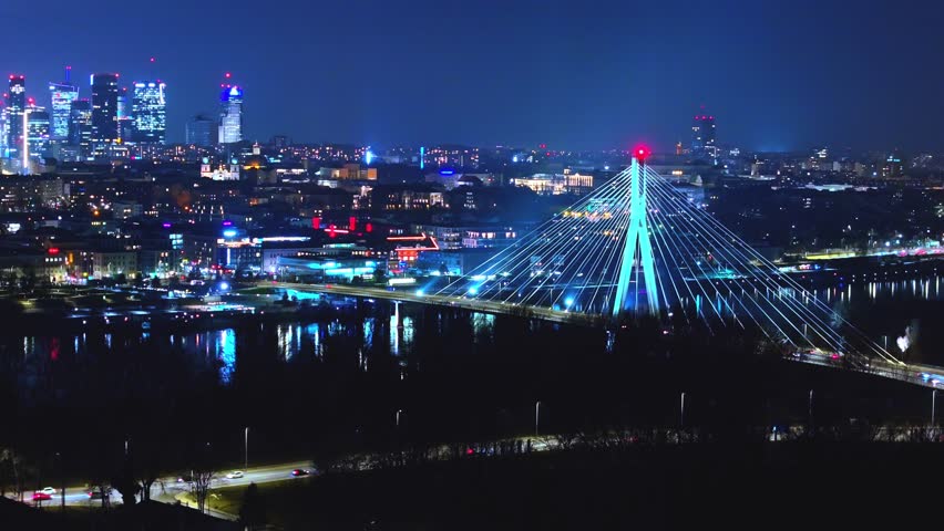 A mesmerizing Warsaw night aerial—Świętokrzyski Bridge, shimmering reflections, and the glowing urban sprawl.
