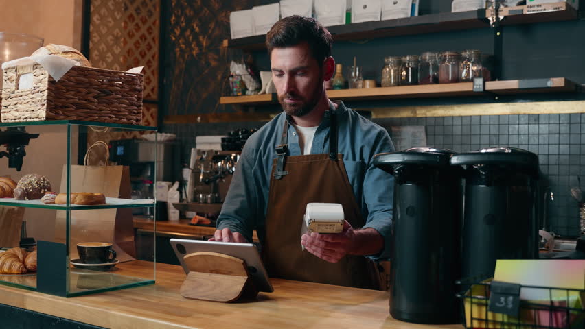 Carefree Caucasian guy entrepreneur owner worker make order client payment buy device tablet in coffee shop small business barista smile delivery cafeteria adult man waiter working in cafe restaurant