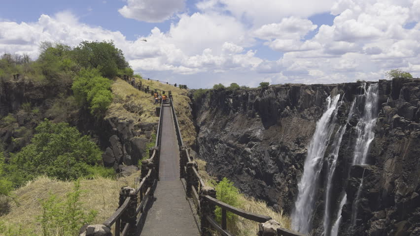 Walking tourist POV Victoria Falls Zambia, the cascading water and expansive gorge viewed from the walking bath bridge