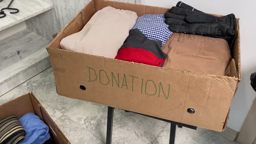 Close-up a several cardboard boxes with things, with an empty clothes closet in the background. Winter and summer clothes. Help for poor and needy people.
