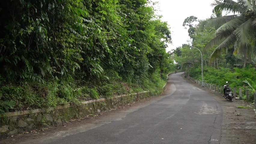 a villager carries grass on a motorbike through an uphill road behind a hill
