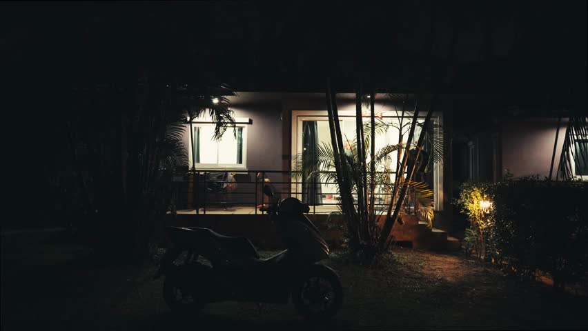 A man exits his house in the dark of night. He approaches a parked motorcycle, climbs on, and swiftly rides away into the night, breaking the stillness of the surroundings.