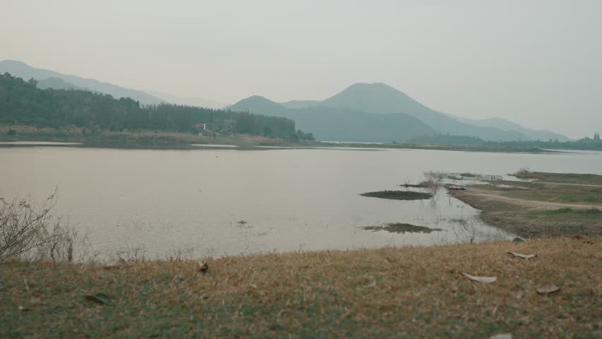 Back view of a male traveler sitting on a camping chair, gazing at the mountain and lake view, surrounded by serene nature