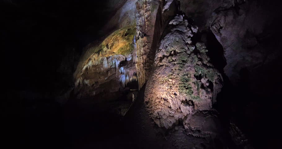 A captivating view of a dark limestone cave with dramatic stalactites hanging from the ceiling and stalagmites rising from the floor, illuminated by artificial light, showcasing natural formations