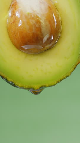 Oil is dripping down from cut in half avocado fruit. Conceptual slow motion vertical template.