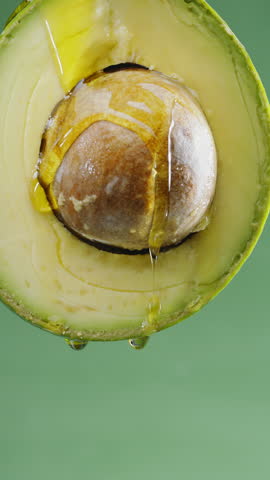 Oil is dripping down from cut in half avocado fruit. Conceptual slow motion vertical template.