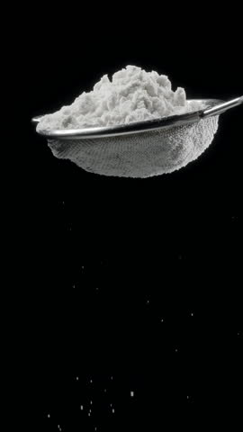 Sift icing sugar or powdered sugar through a sieve tool on black background.