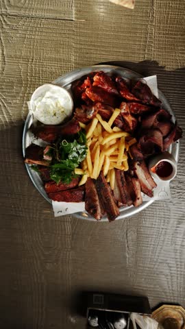Mouthwatering barbecue platter features ribs, brisket, and fries served with tangy sauce and creamy dip in bustling restaurant