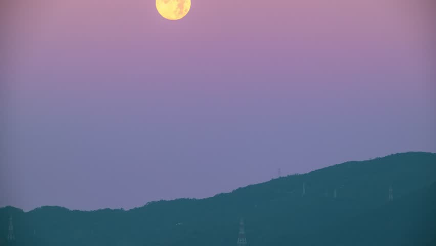 A full moon setting behind the silhouette of XiZhi DaJian Mountain under a pink and orange dawn sky. Spring morning, New Taipei City, Taiwan.