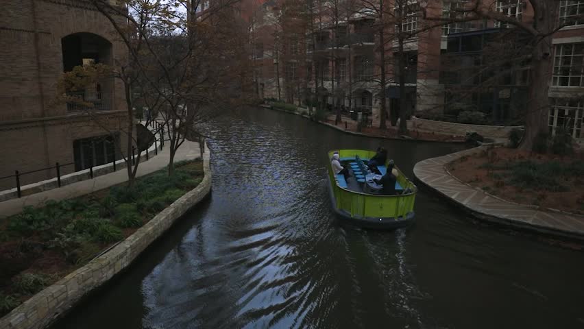 A smooth motion shot follows a tour boat drifting through the river, surrounded by towering buildings, capturing the perfect blend of urban life and tranquil waters.
