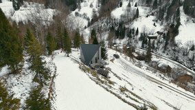 Modern A-frame cabin on a snowy hillside, surrounded by pine trees, with a panoramic view of scattered rural houses. A black car is parked near the house on a snow-covered path - Powered by Shutterstock - Get 15% off with code: PIKWIZARD15