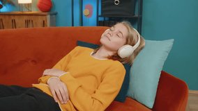 Caucasian teenager boy listens to an audiobook using wireless headphones at home. Relaxedly child lies on sofa, engages with audio lessons to learn a language, enjoying music and studying at home room - Powered by Shutterstock - Get 15% off with code: PIKWIZARD15