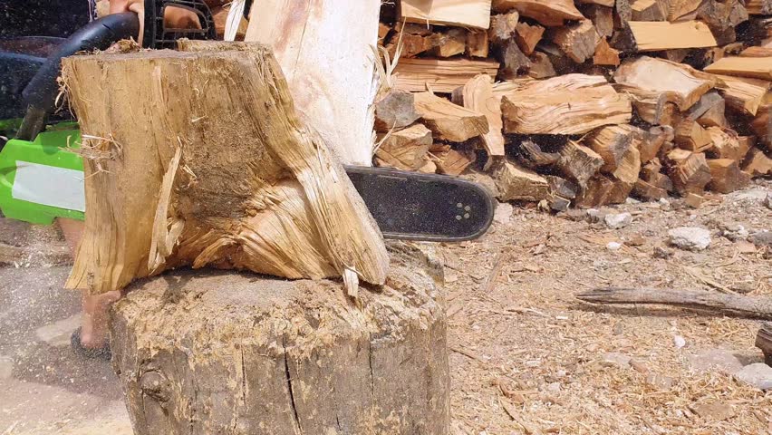 Close up of lumberjack or logger hands sawing firewood for logs using his chainsaw. Woodcutter working and sawdust fly to sides.