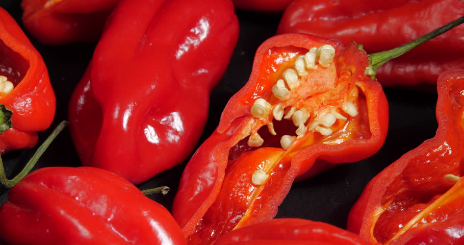 Red Hot Cayenne Habanero Pepper and Halves with Seeds Rotating Slowly Along the Frame on a Black Stone Background. Spicy Food Culinary Ingredient