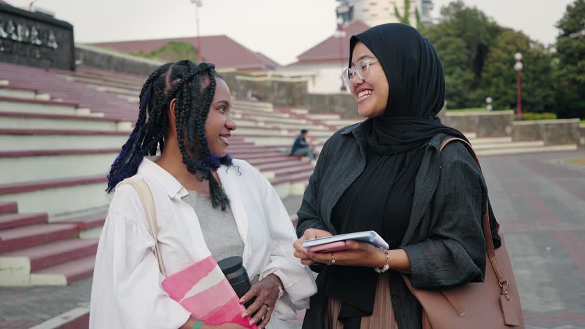 Two diverse Asian student girl friends talking and laughing outdoors smiling at the camera. Diversity in Indonesia