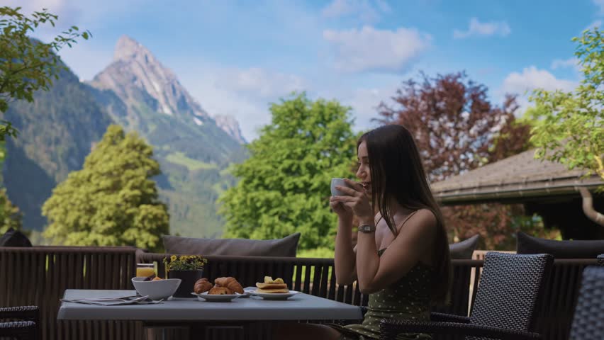 Tourist beautiful woman drinking coffee at breakfast on a terrace with a stunning view of the Alps at sunrise. Perfect for lifestyle and vacation concepts in Switzerland  
