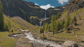 Establishing aerial view of a tourist active man with a backpack hiking towards towards scenic waterfall in Swiss Alps. Perfect for lifestyle, travel, vacation, and adventure in the Switzerland  - Powered by Shutterstock - Get 15% off with code: PIKWIZARD15
