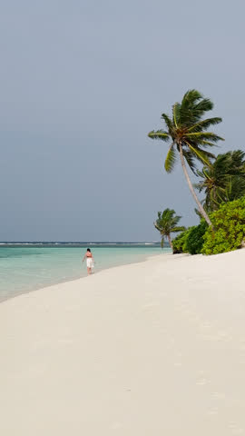 a girl walks on the beach on the amazing wild beach of the island of Maldives in the Indian Ocean. Azure water and palm trees. Palm shadow on the white sand