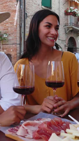 Vertical HD video of three happy diverse women having fun together enjoying red wine at restaurant during summer vacation in Italy. Friendship, leisure and travel concept.