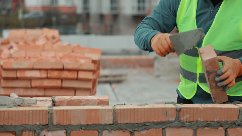 Construction worker laying bricks on a wall, Close-up of a construction worker building a brick wall with a trowel on a construction site.