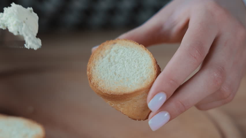 Spreading soft cheese on a slice of toasted bread, Close-up of a knife spreading soft cheese on a toasted bread slice.