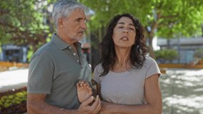 Middle-aged couple having a serious discussion outdoors in a city park, capturing emotions and relationship dynamics amidst a lush urban backdrop. - Powered by Shutterstock - Get 15% off with code: PIKWIZARD15