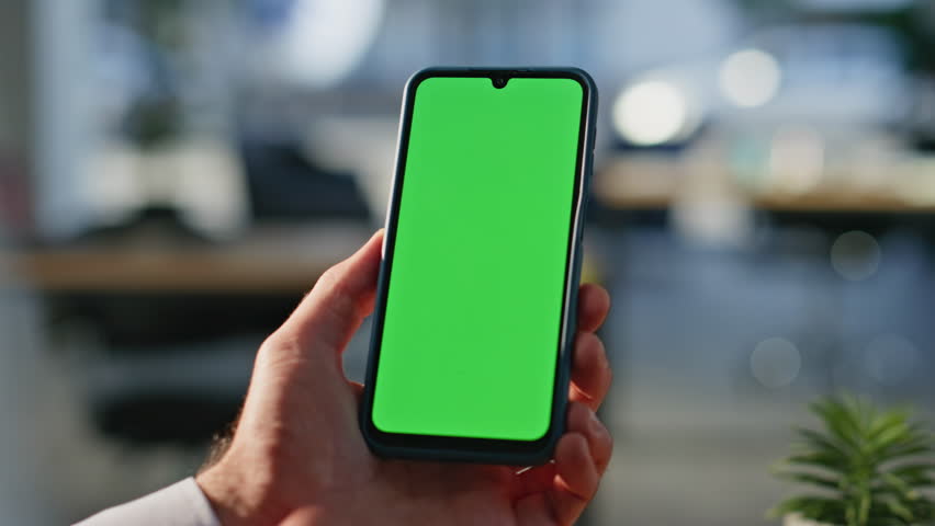 Businessman using chromakey smartphone making online order at workplace closeup. Unknown man hand tapping green screen cellphone in office. Male manager browsing email on mockup mobile phone indoors.