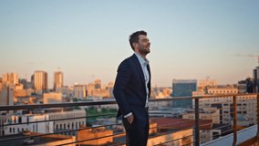 Smiling ceo relaxing at outdoors terrace contemplating sunset cityscape. Happy businessman wearing elegant suit standing at balcony railings. Successful business owner looking city in evening light. - Powered by Shutterstock - Get 15% off with code: PIKWIZARD15