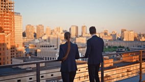 Business people standing terrace looking at modern cityscape in golden sunset sunlight back view. Elegant colleagues talking on office balcony. Successful partners discussing work on urban rooftop. - Powered by Shutterstock - Get 15% off with code: PIKWIZARD15
