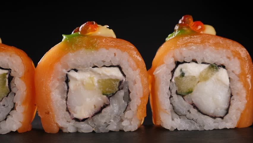 Sushi rolls on black platter over dark background, closeup. Japanese cuisine
