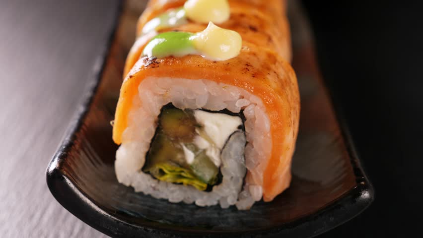 Sushi rolls with tuna and salmon with roe on black platter, closeup. Japanese cuisine