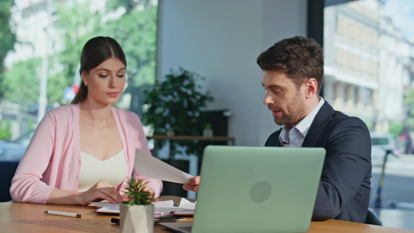 Woman client analyzing documents talking with professional manager in modern office. Financial consultant discussing project strategy at business meeting. Lady signing agreement shaking hand partner.