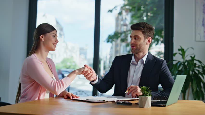 Woman client analyzing documents talking with professional manager in modern office. Financial consultant discussing project strategy at business meeting. Lady signing agreement shaking hand partner.